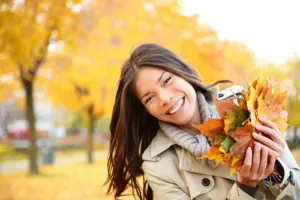 Smiling woman in coat playing with leaves during fall